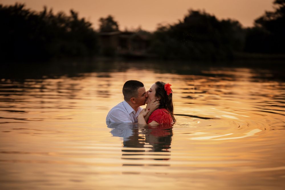 Couple embraces while standing in lake water during romantic sunset photoshoot.