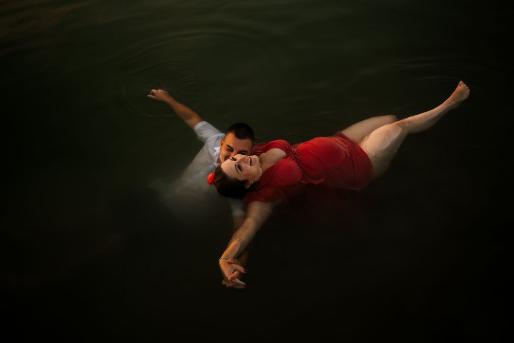 Figure in red dress floats gracefully with outstretched arms in dark water.