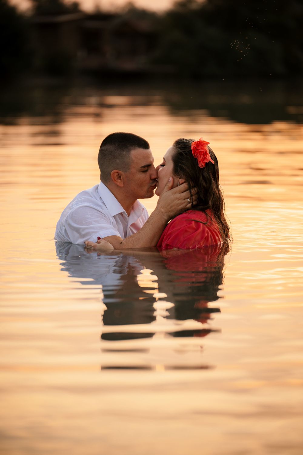 A romantic couple shares an intimate moment while standing in water during golden hour sunset.