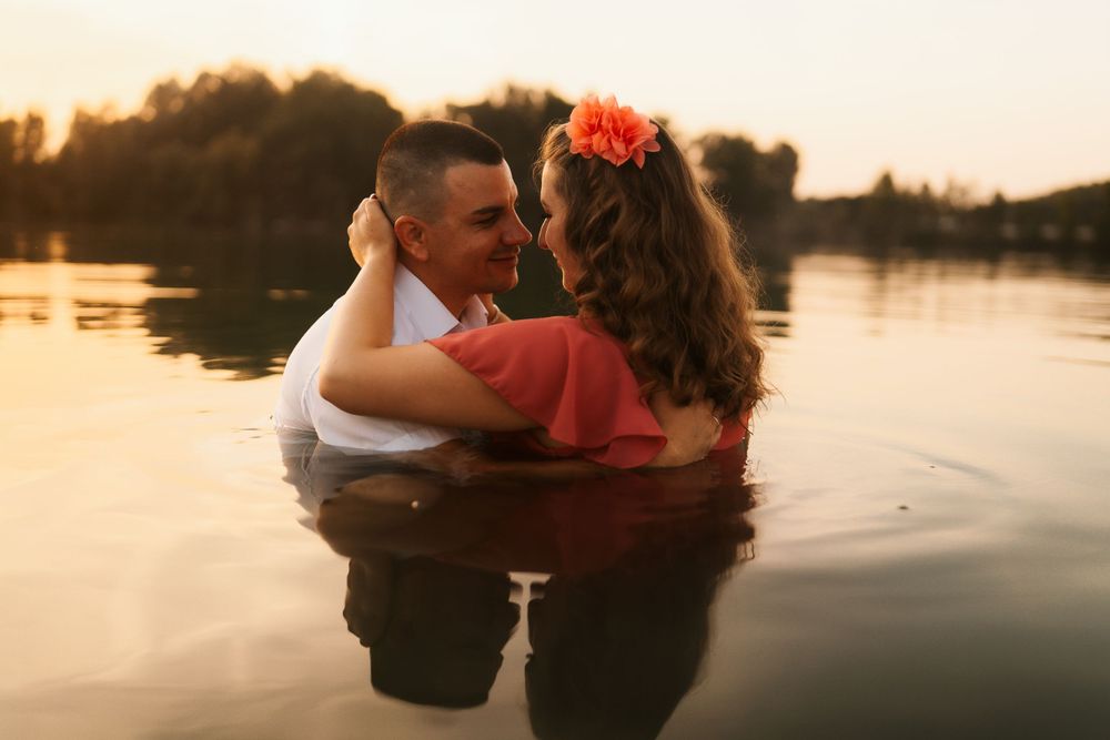 A couple embraces while standing in lake water during a warm sunset.