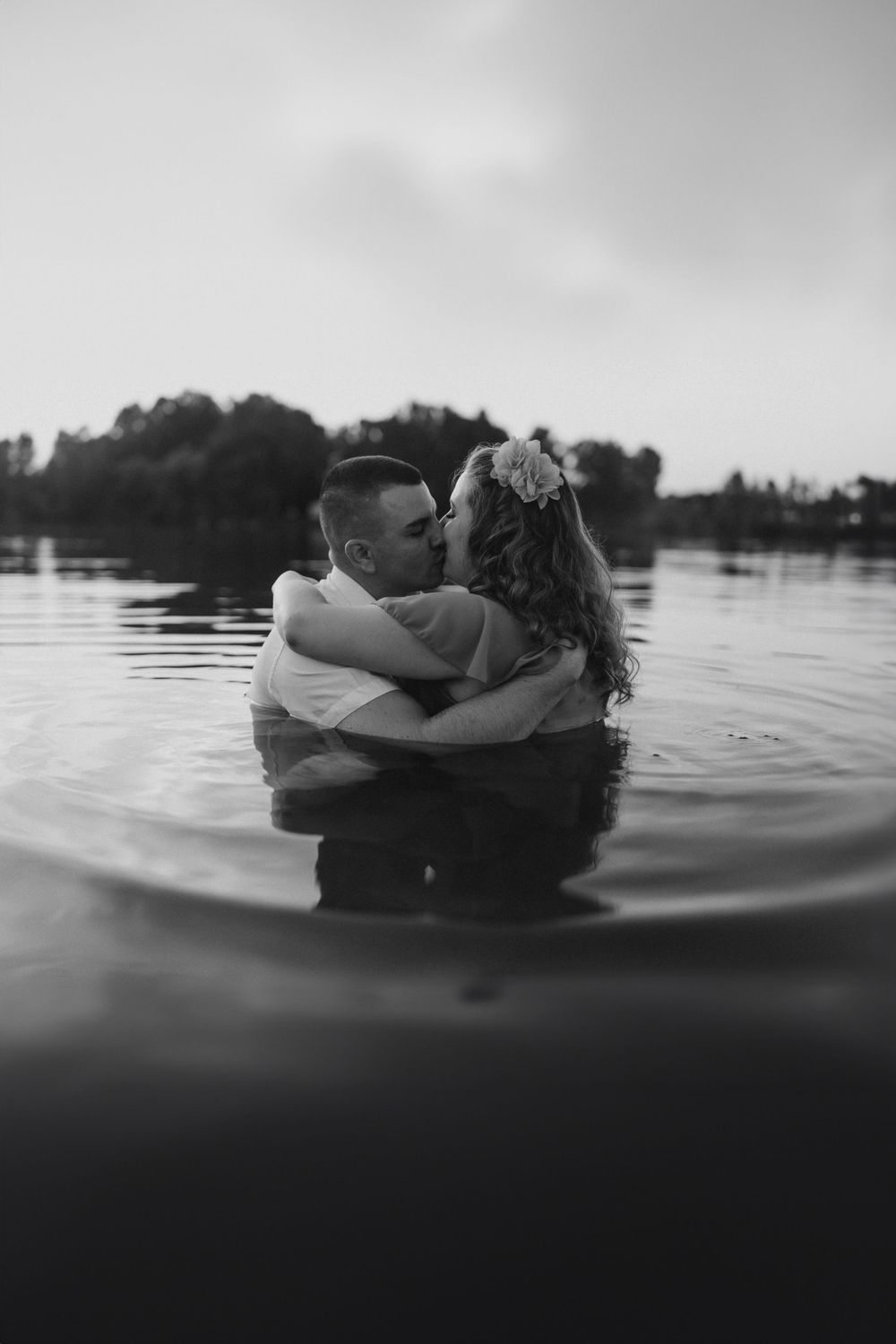 Intimate black and white portrait of couple embracing in calm lake waters.