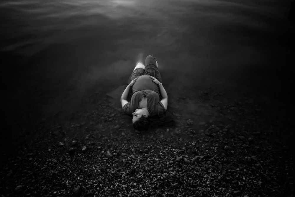 Dark underwater portrait shows a figure floating near the rocky bottom.