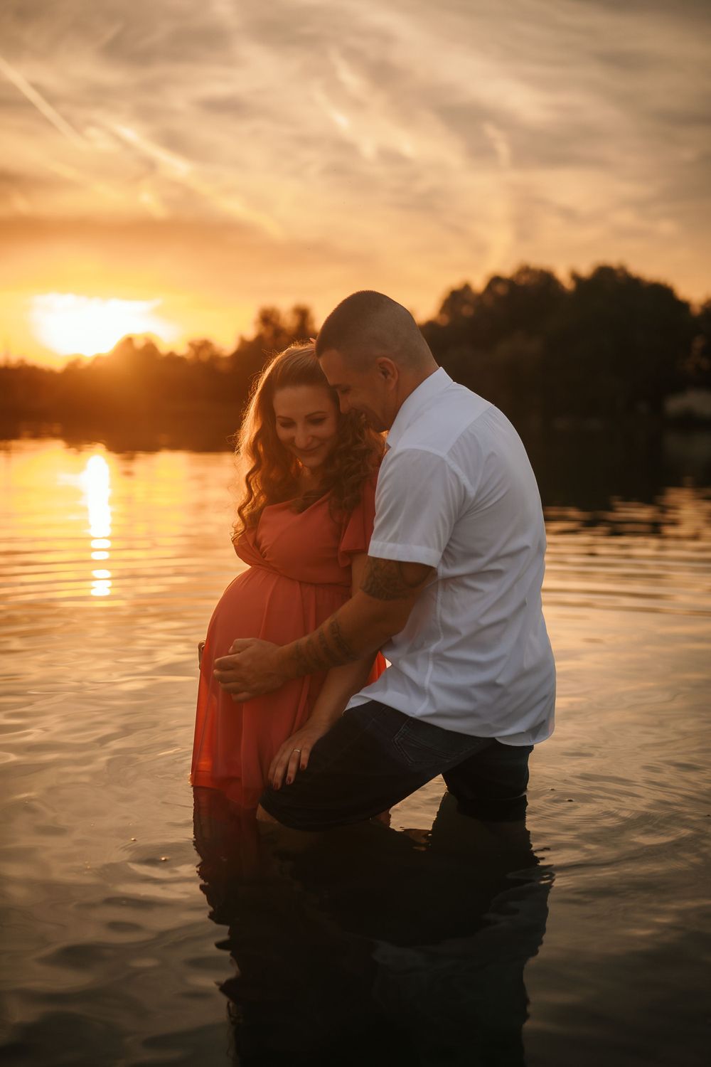 A couple shares an intimate moment standing in water during a golden sunset.