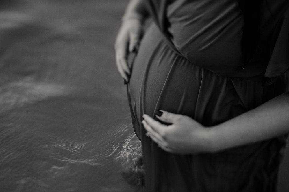Close up black and white photo of pregnant belly with hands gently resting on top.