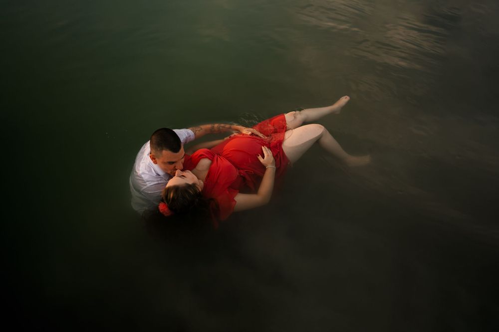 A figure in a red dress floats gracefully underwater in a dark and moody underwater portrait.