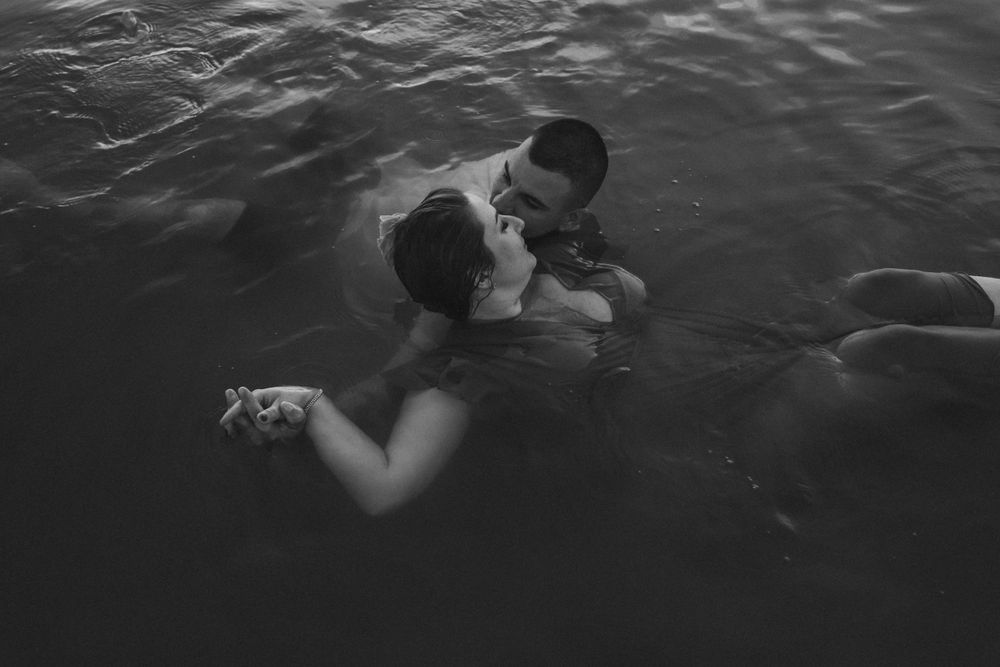 A couple embraces while floating in dark water during an intimate photoshoot.