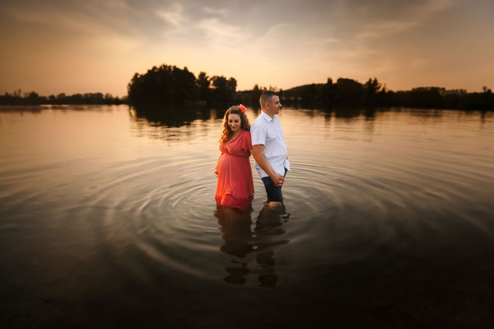 A couple creates ripples while standing in a lake during a golden sunset.
