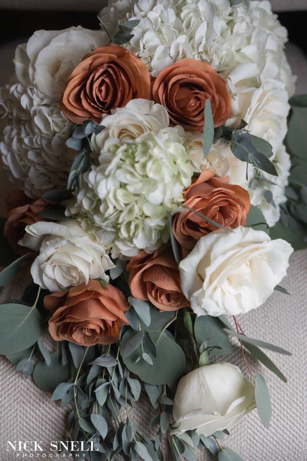 Wedding bouquet featuring white hydrangeas, coral roses, and eucalyptus leaves.