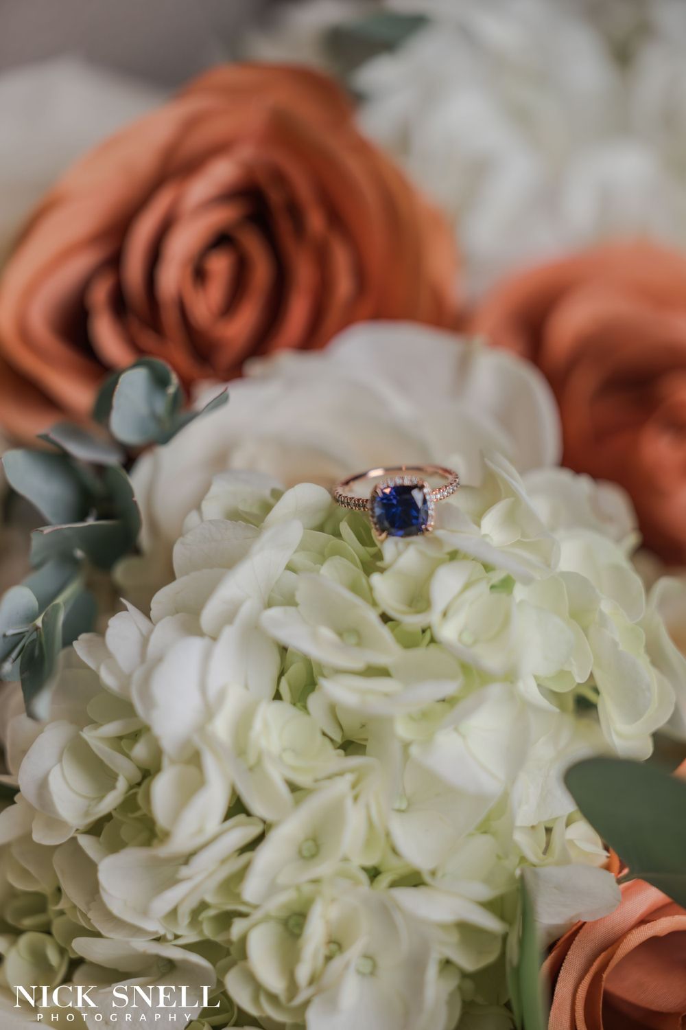 White hydrangeas and coral roses arranged with eucalyptus leaves in a wedding bouquet.