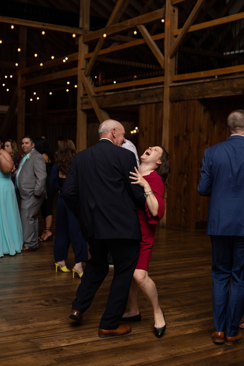 Couples dancing and celebrating in rustic barn venue with string lights overhead.