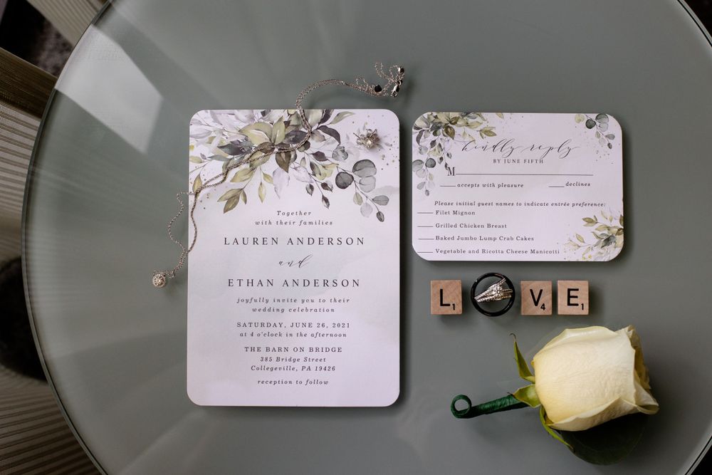 Wedding invitation suite with floral design and LOVE letter blocks on gray surface.