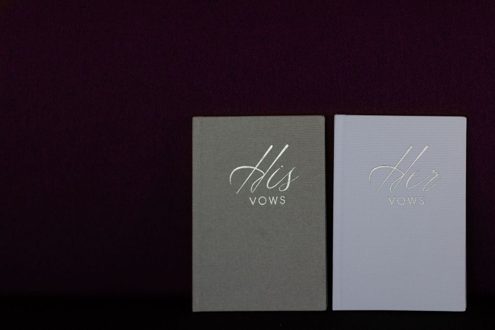 His and hers vow books photographed against dark background.