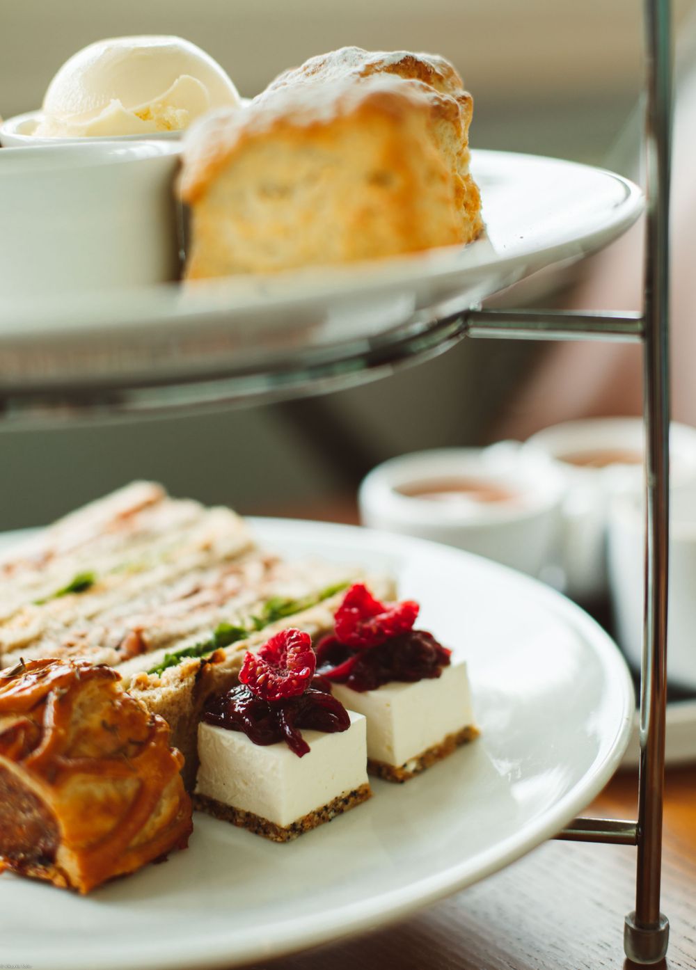 Close-up view of gourmet desserts and sandwiches arranged on white tiered plates with garnishes.