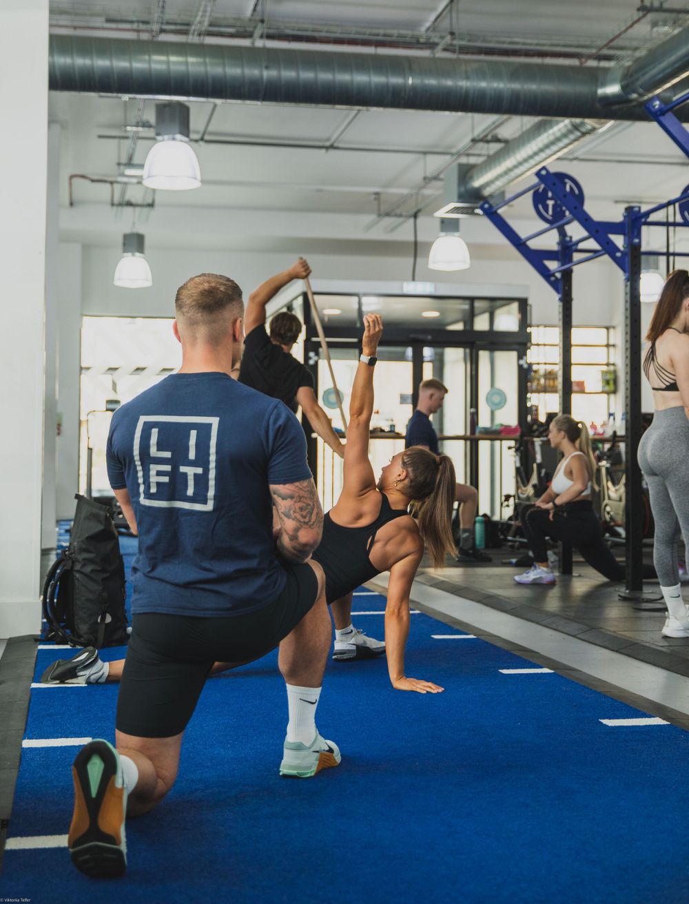 Group fitness class exercising in a modern gym with blue flooring.