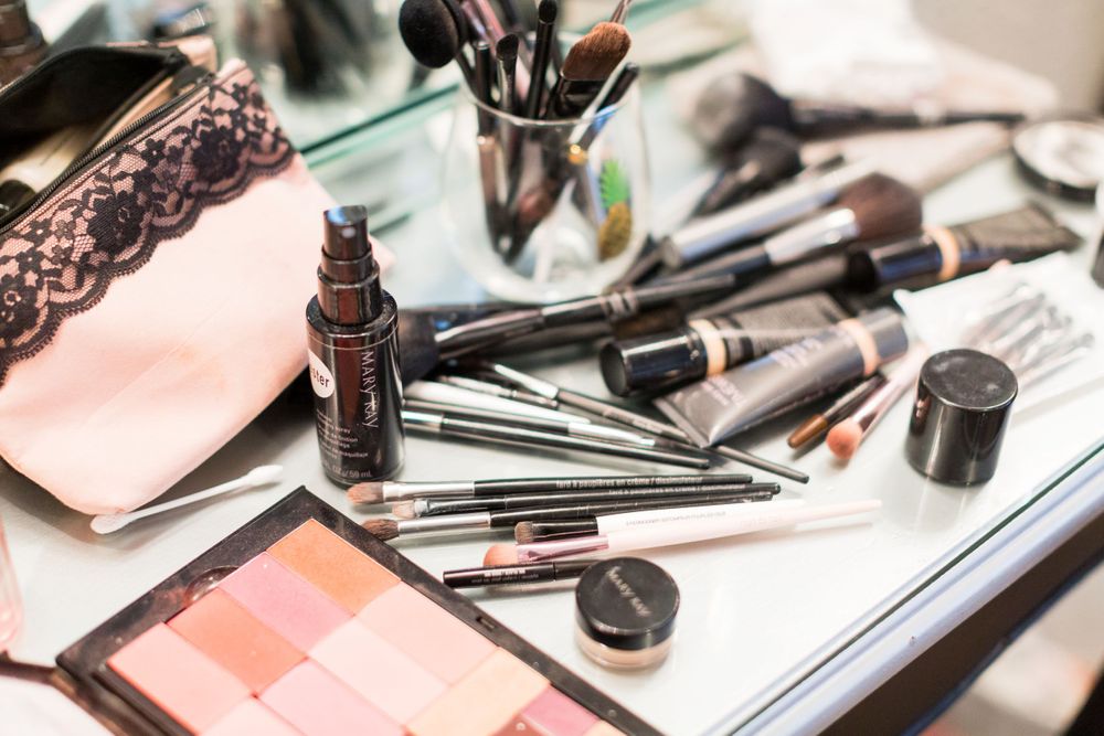 Various makeup brushes, cosmetics and beauty products arranged on a light surface.