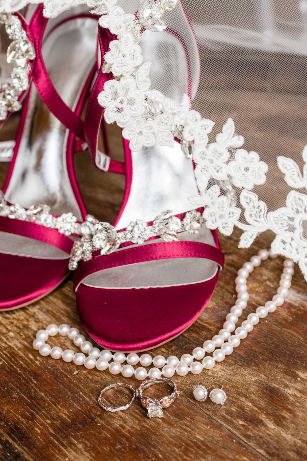 Red bridal heels with lace details and pearl accessories on a wooden surface.