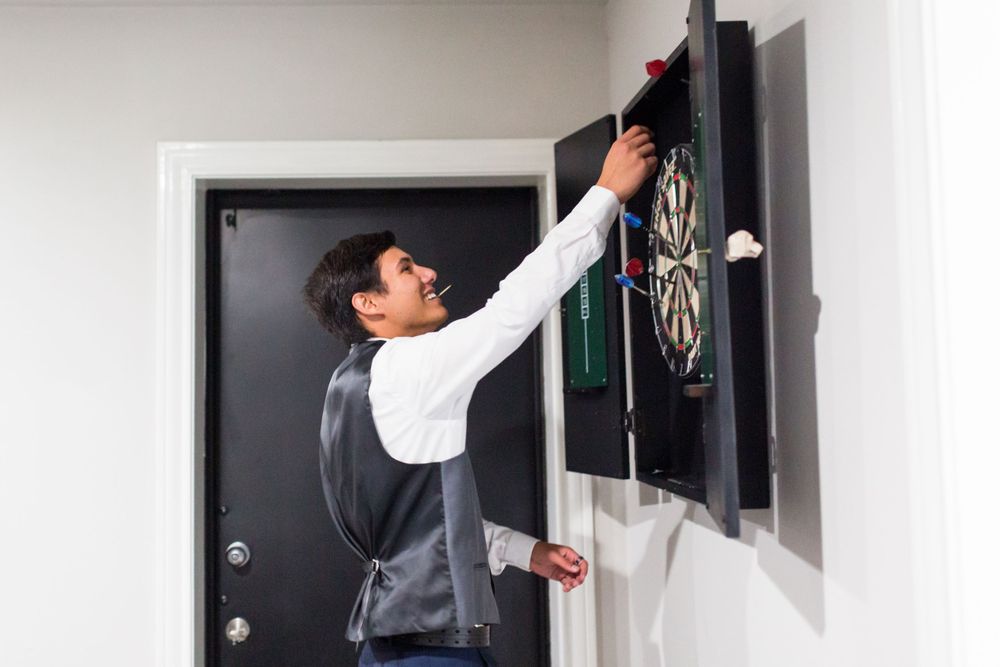 Person in formal attire reaching up to adjust a mounted dartboard on a wall.