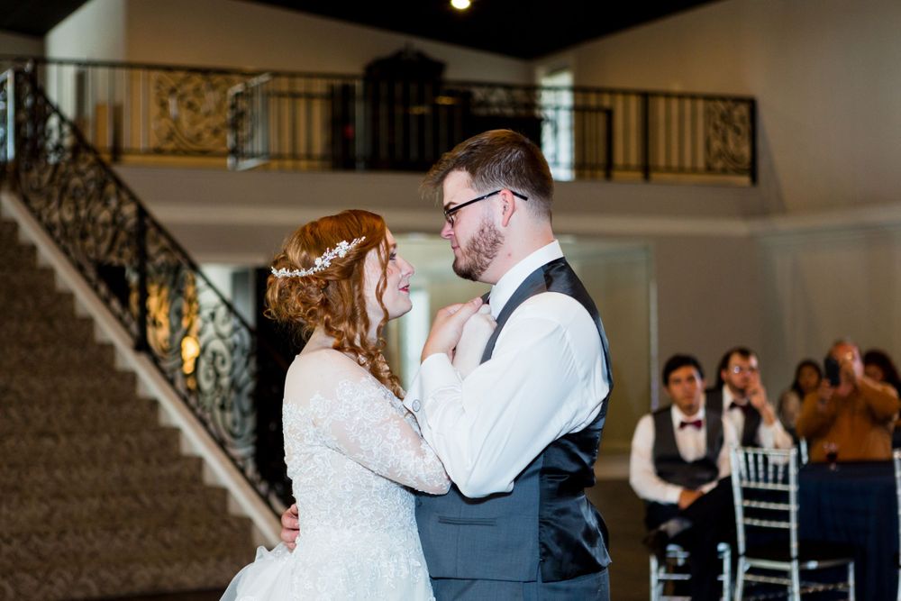 A couple dancing in an elegant venue with guests watching from behind.