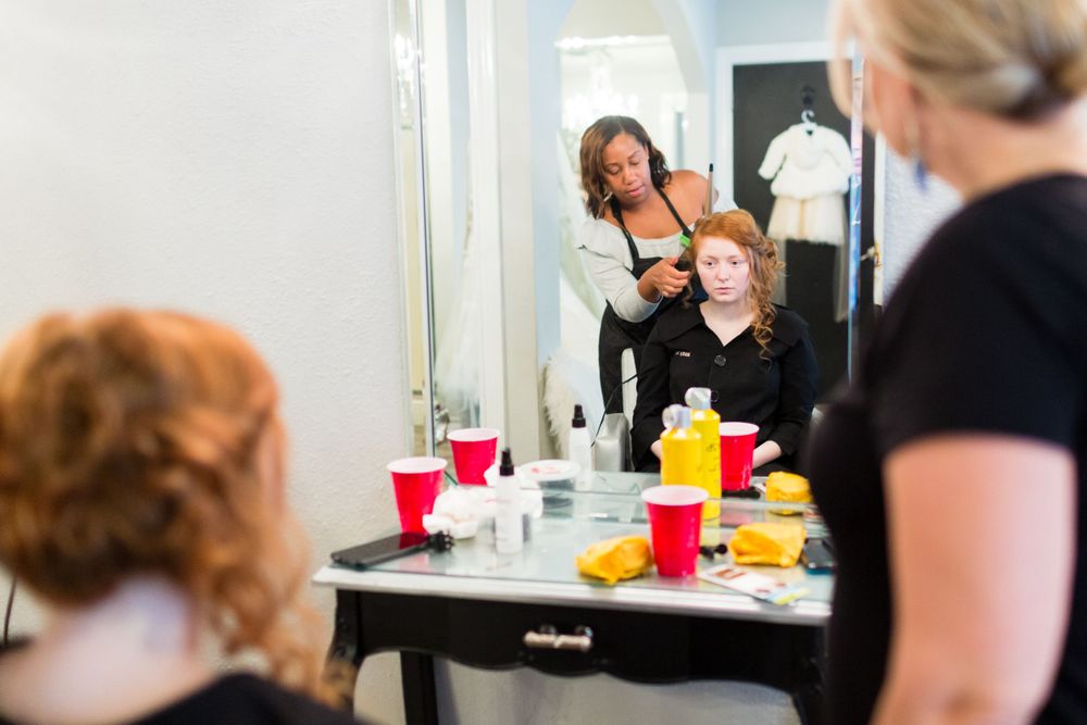 Professional makeup session in progress at a beauty salon with bright lighting and mirrors.
