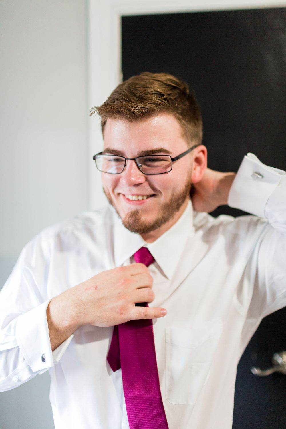 Person adjusting a burgundy tie while getting dressed.
