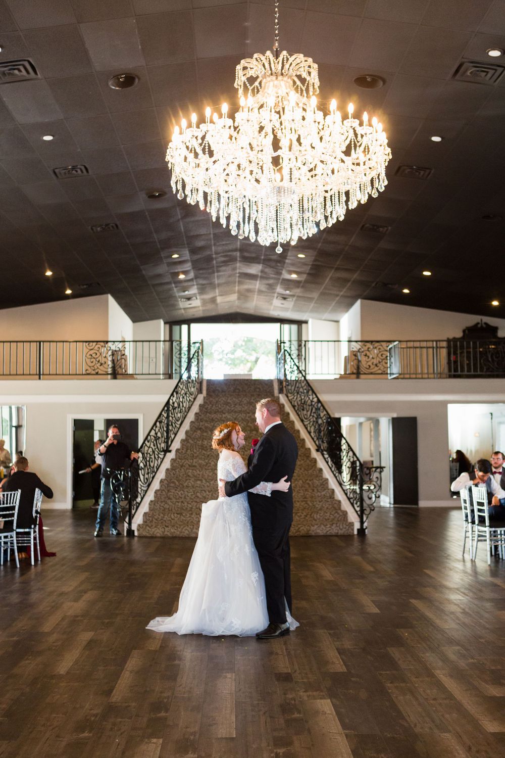 A romantic dance moment under a grand crystal chandelier in a spacious ballroom.