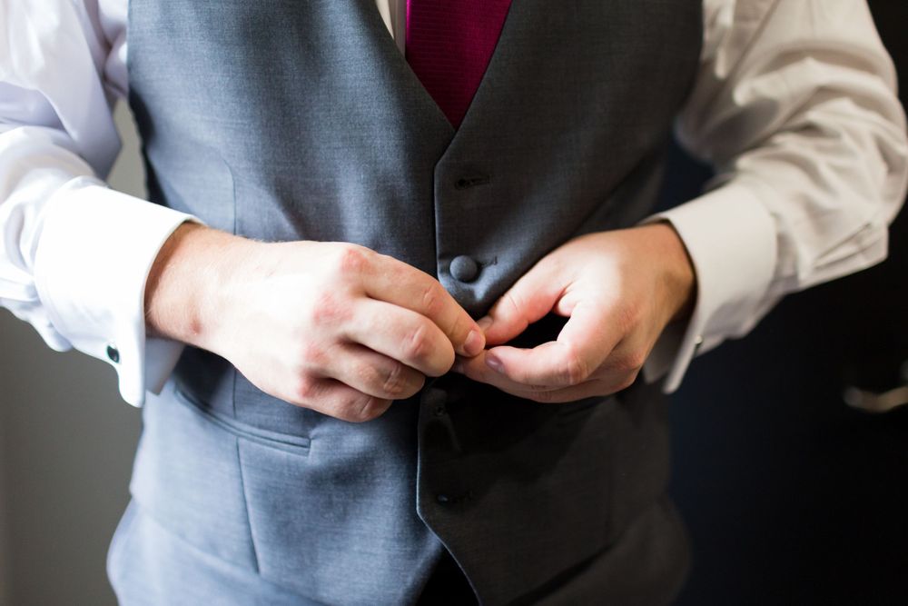 Close-up of hands buttoning a gray formal vest.