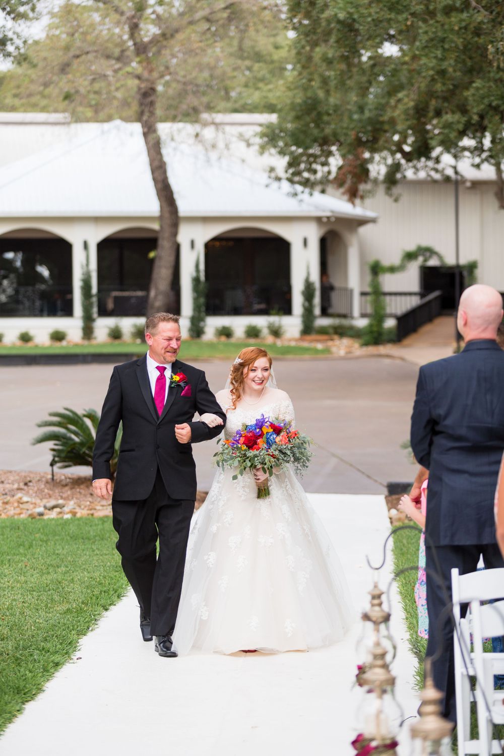 Wedding processional on white walkway with couple walking past decorative columns.