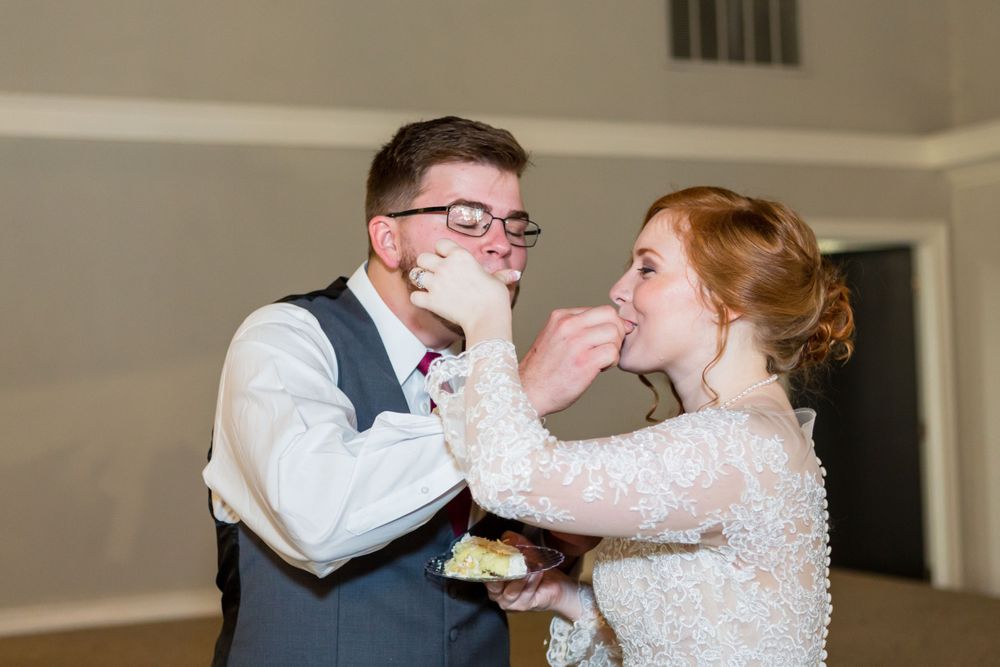 A joyful wedding couple playfully feed each other cake during their reception celebration.
