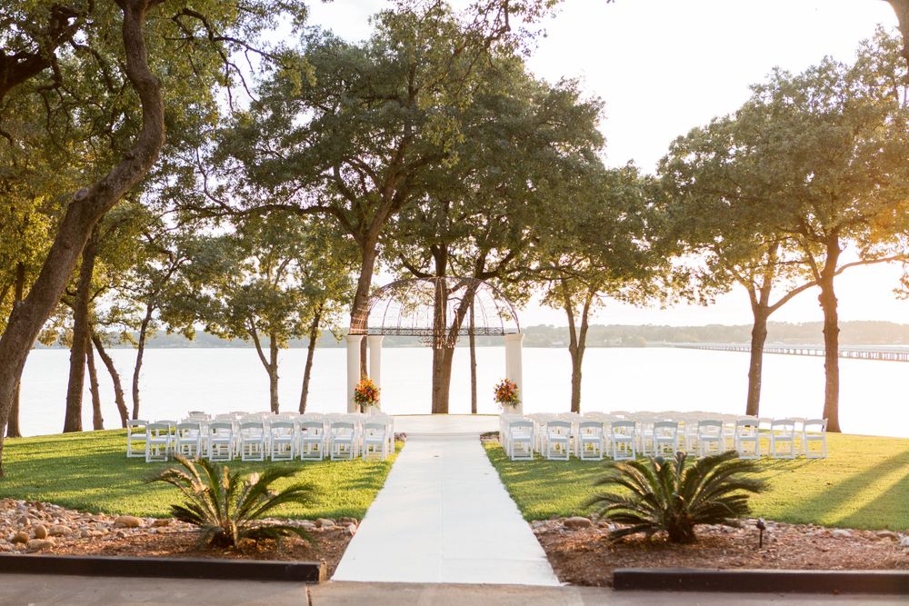 Waterfront wedding ceremony setup with white chairs and aisle facing a lake at sunset.