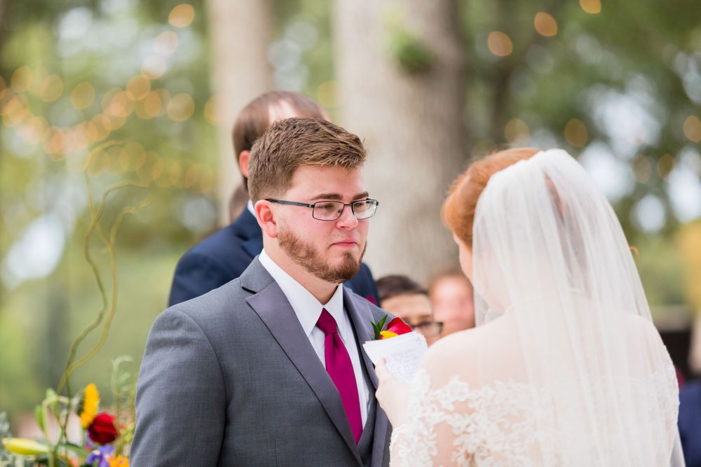 Groom in grey suit and burgundy tie during outdoor wedding ceremony.