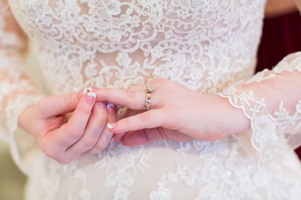 Close-up shot of hands showing a delicate lace wedding dress sleeve and ring detail.