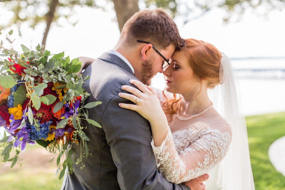 Romantic close-up of couple embracing with colorful bouquet against lakeside setting.