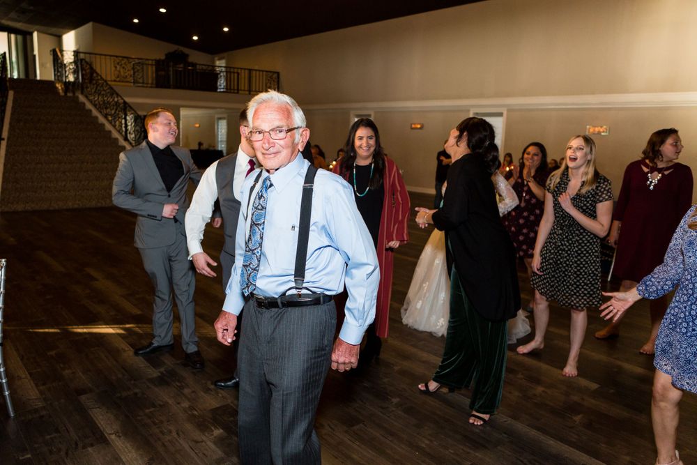 Wedding guests dancing and celebrating on a wooden dance floor under indoor lighting.