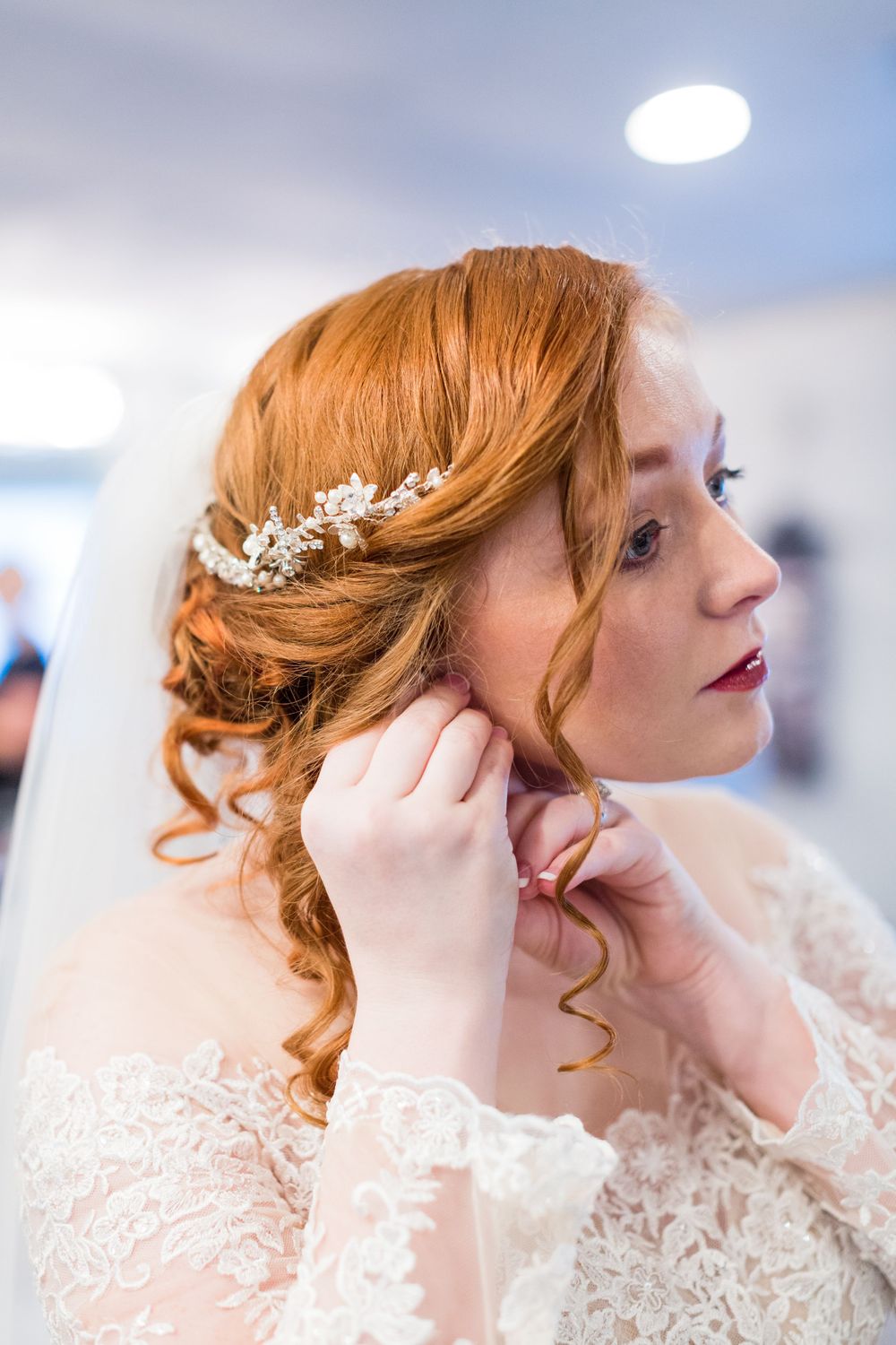A bride with red hair wearing a lace wedding dress and floral hair accessory.