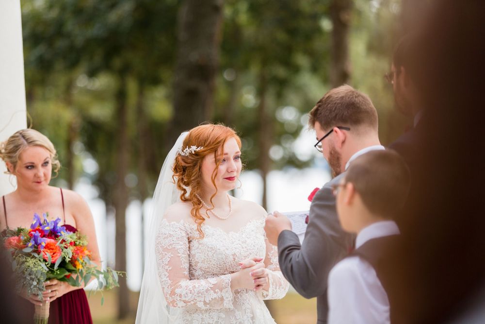Wedding ceremony in progress with attendants and flowers on a lakefront white platform.