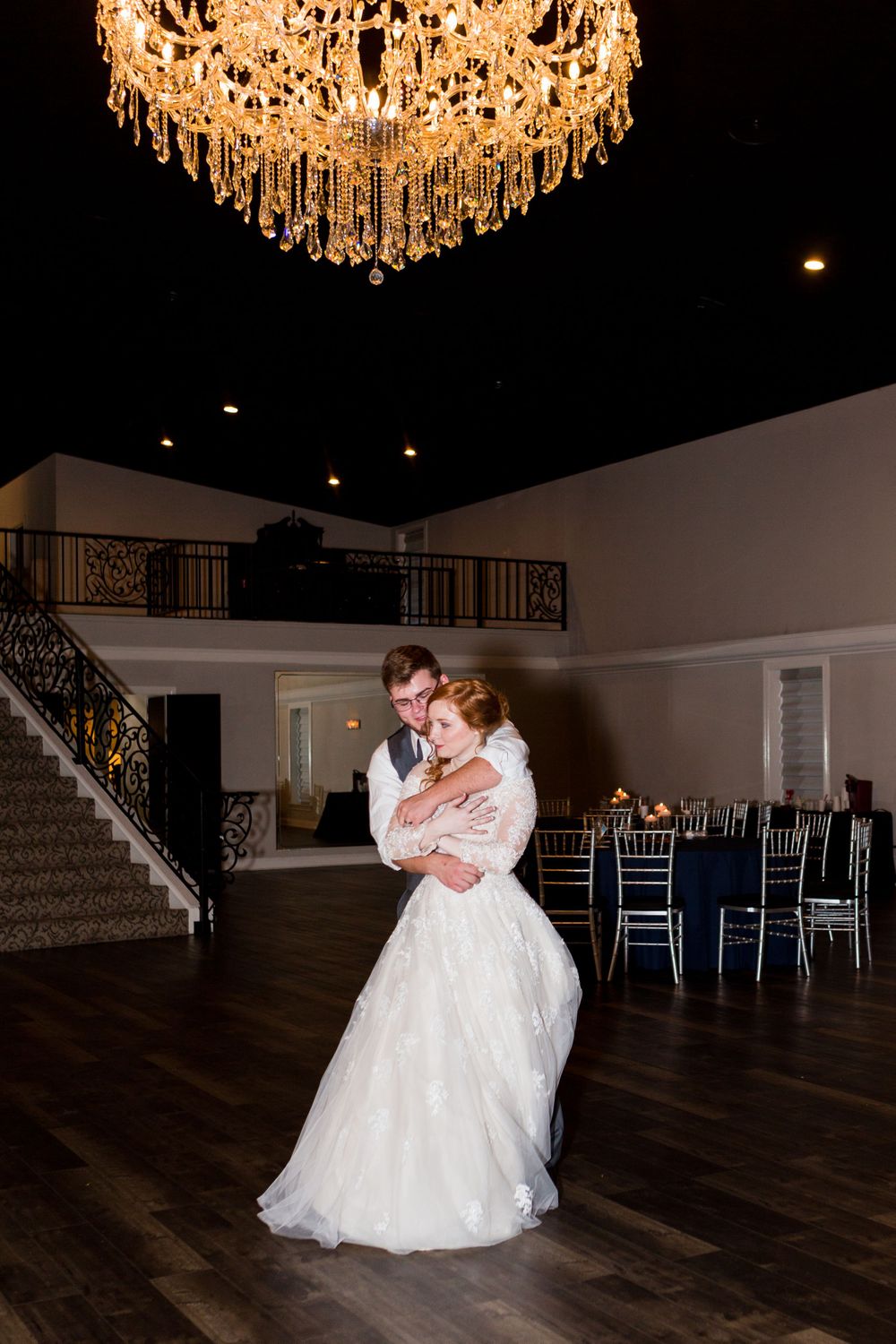 Romantic dance moment under an ornate crystal chandelier in an elegant ballroom setting.