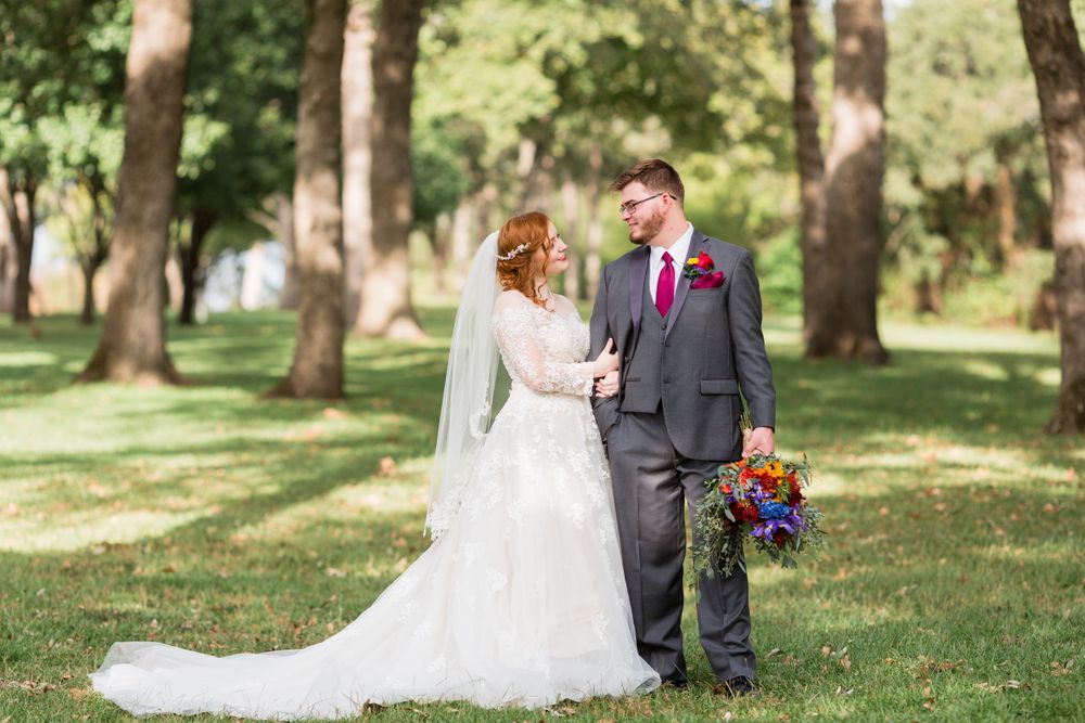 A romantic wedding portrait showing a couple on a grassy lawn with tall trees and natural lighting.