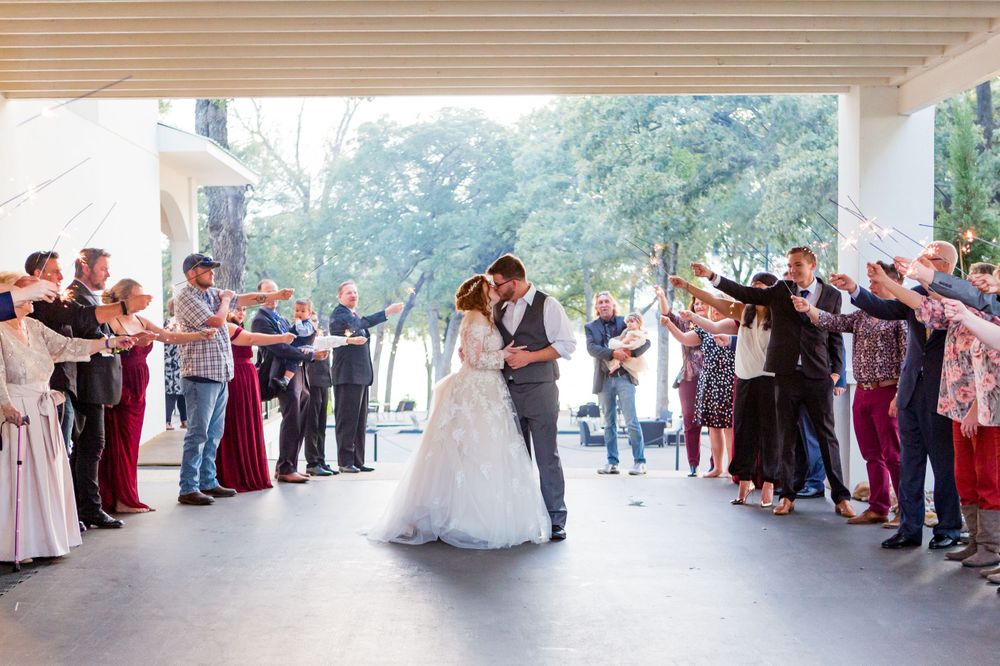Wedding guests form a tunnel as newlyweds share a dance beneath a covered outdoor area.