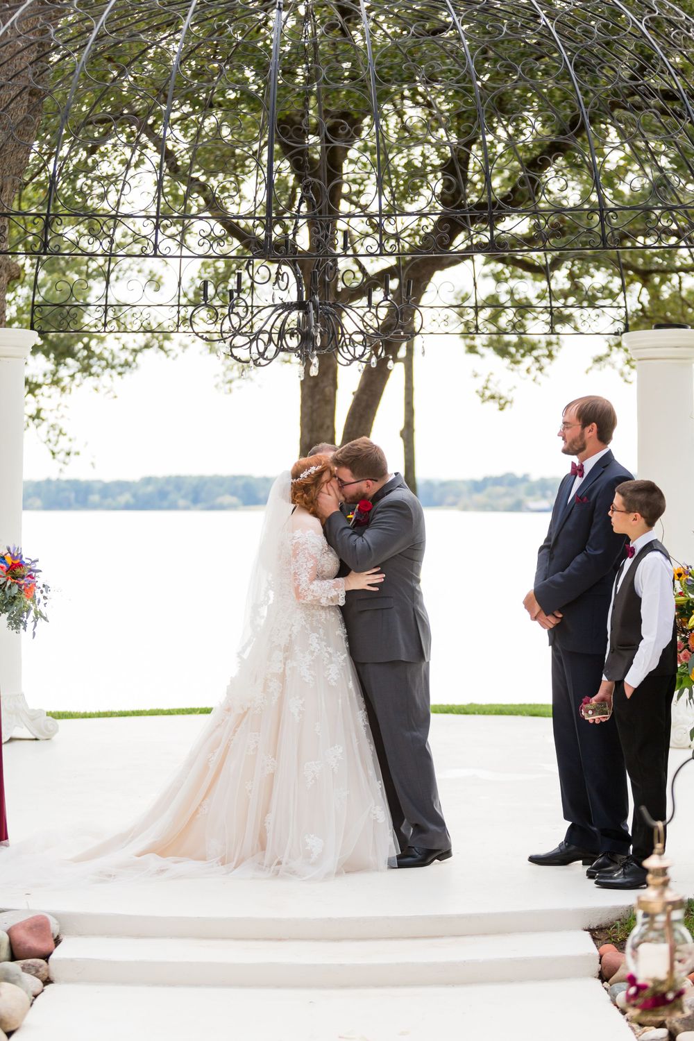 Intimate wedding moment captured under a decorative metal pergola with water views.