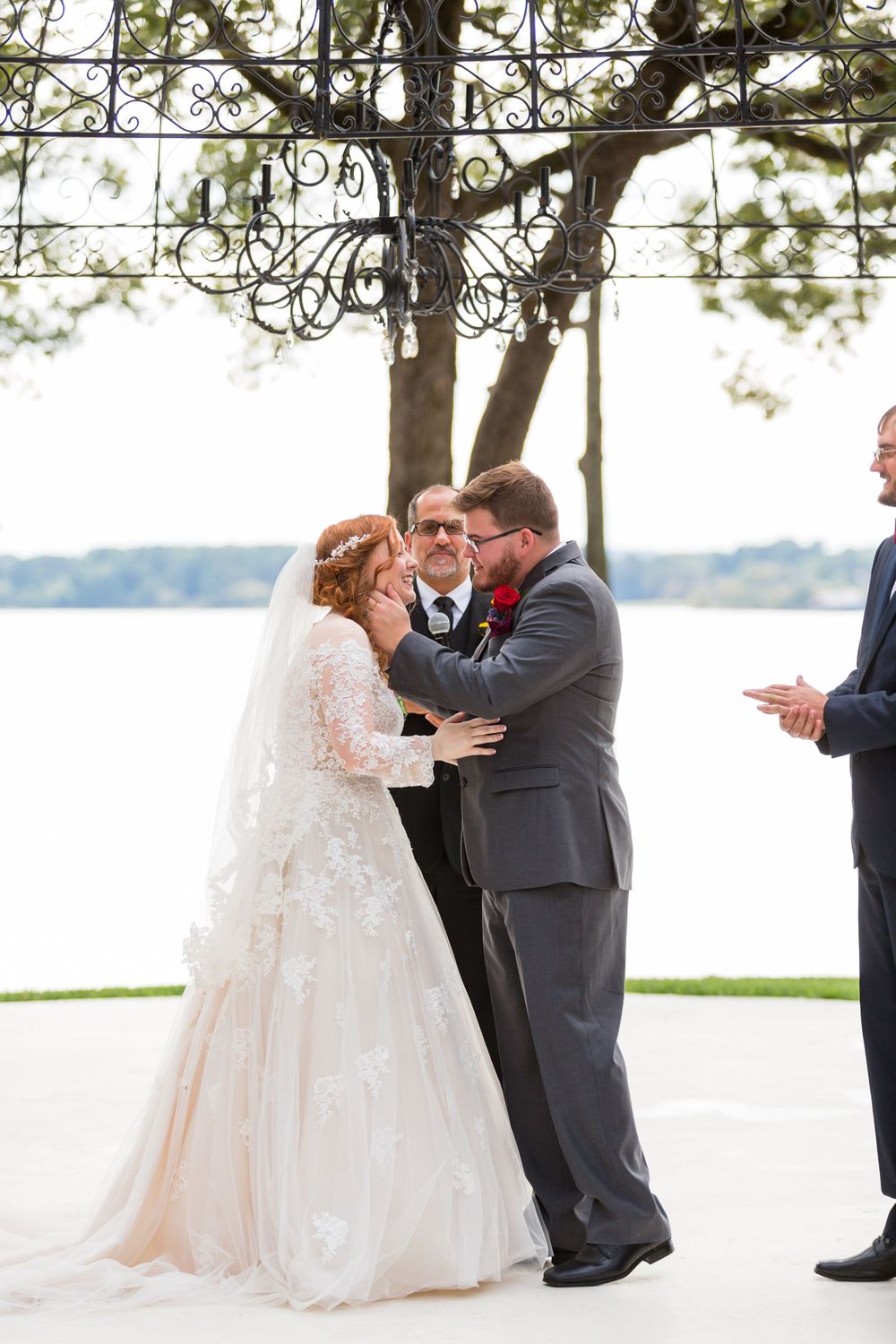 Wedding ceremony kiss under an ornate metal pergola with lake views in the background.