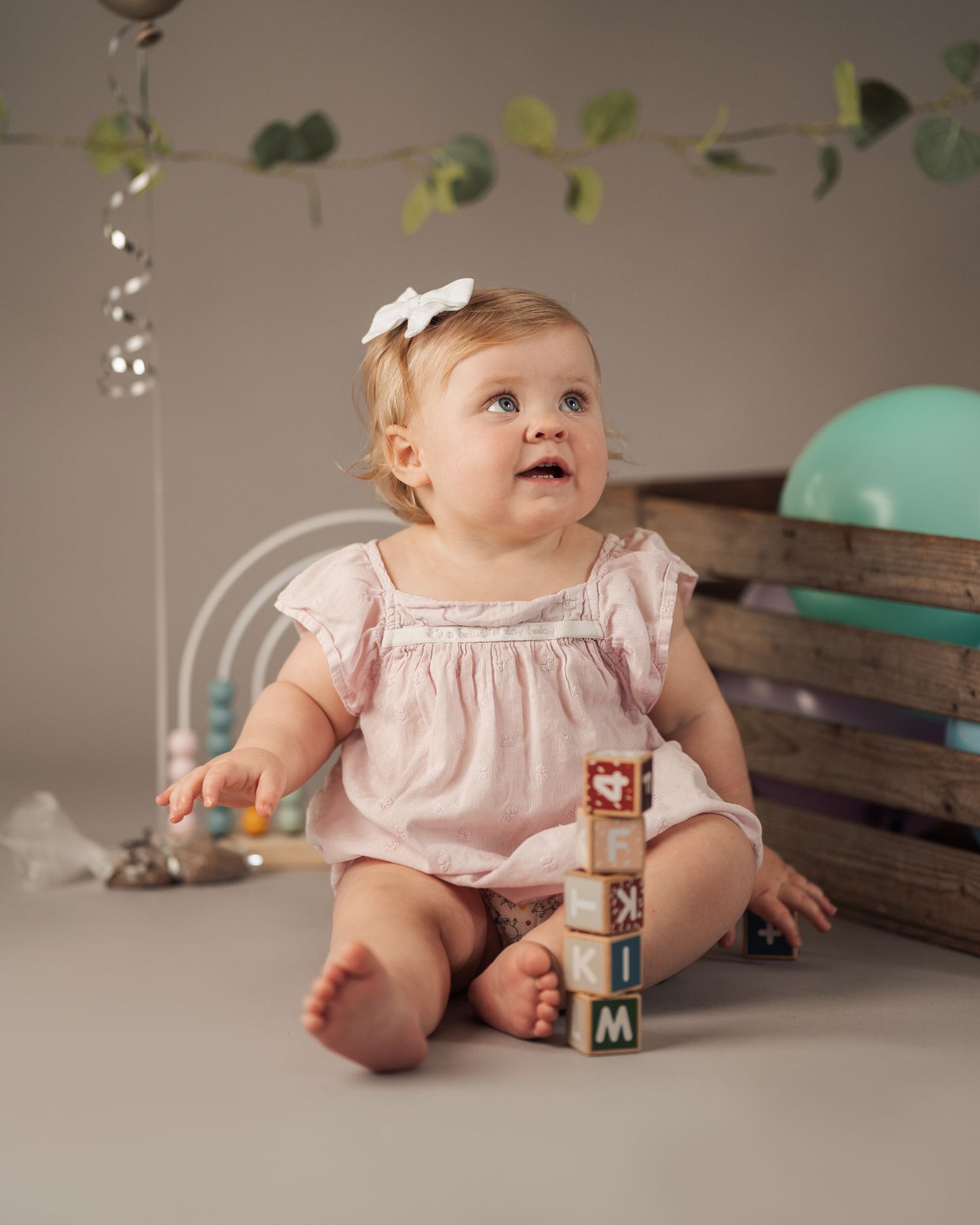 baby i rosa klänning poserar med lekklossar i studio vid babyfotografering