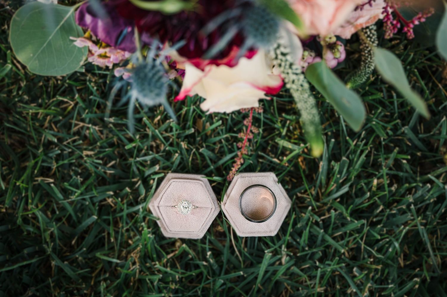 Wedding rings nestled in hexagonal boxes surrounded by greenery and flowers.