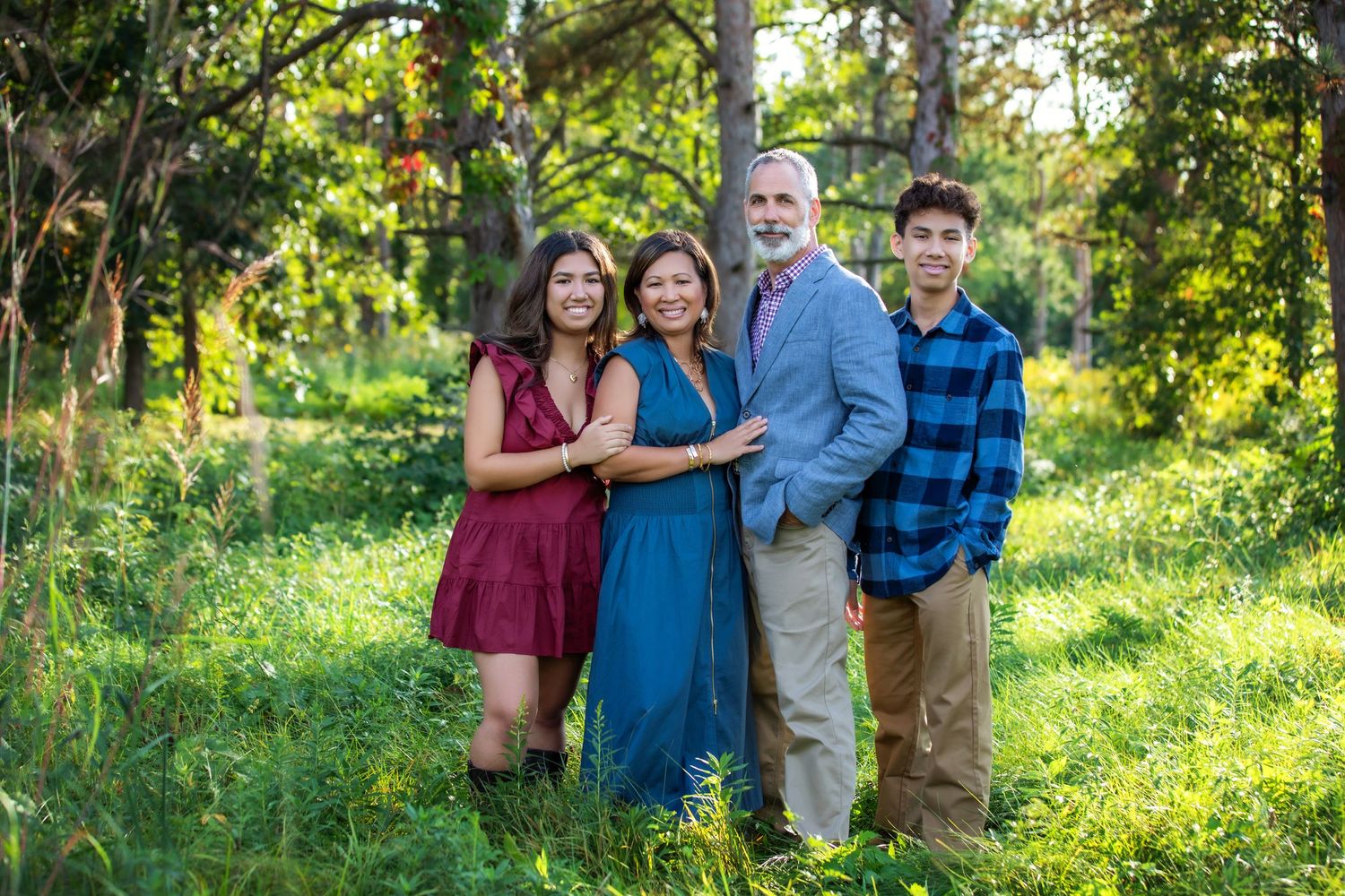 Family group portrait in casual attire standing together in sunlit outdoor setting.