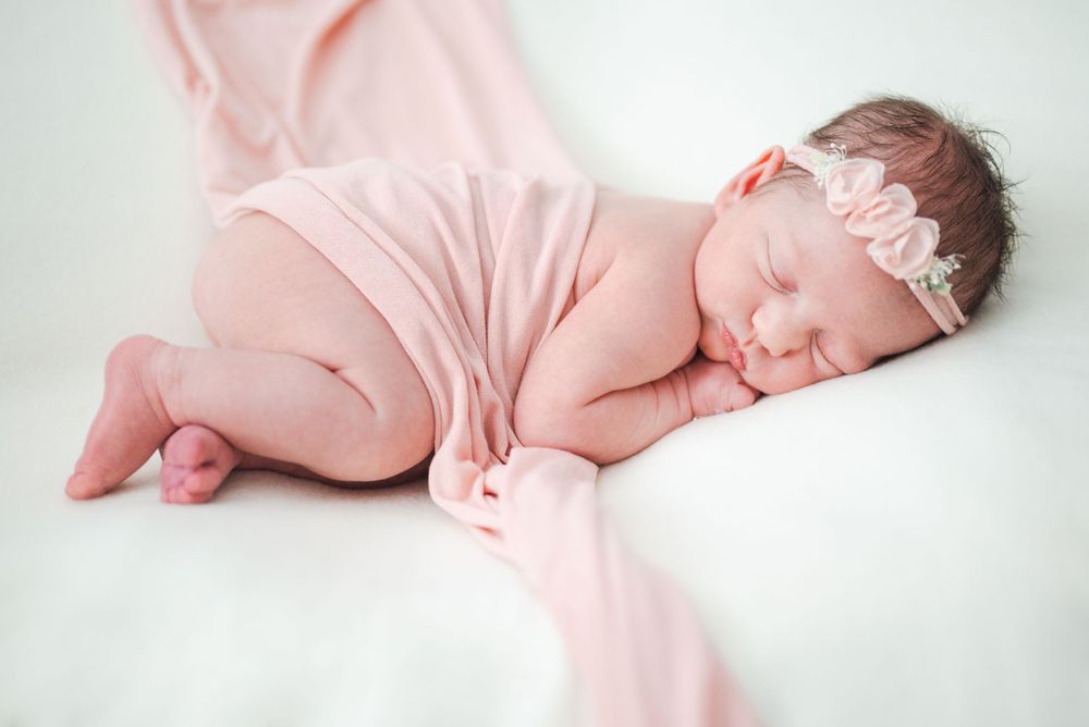 Sleeping newborn wrapped in soft pink fabric with delicate headband.