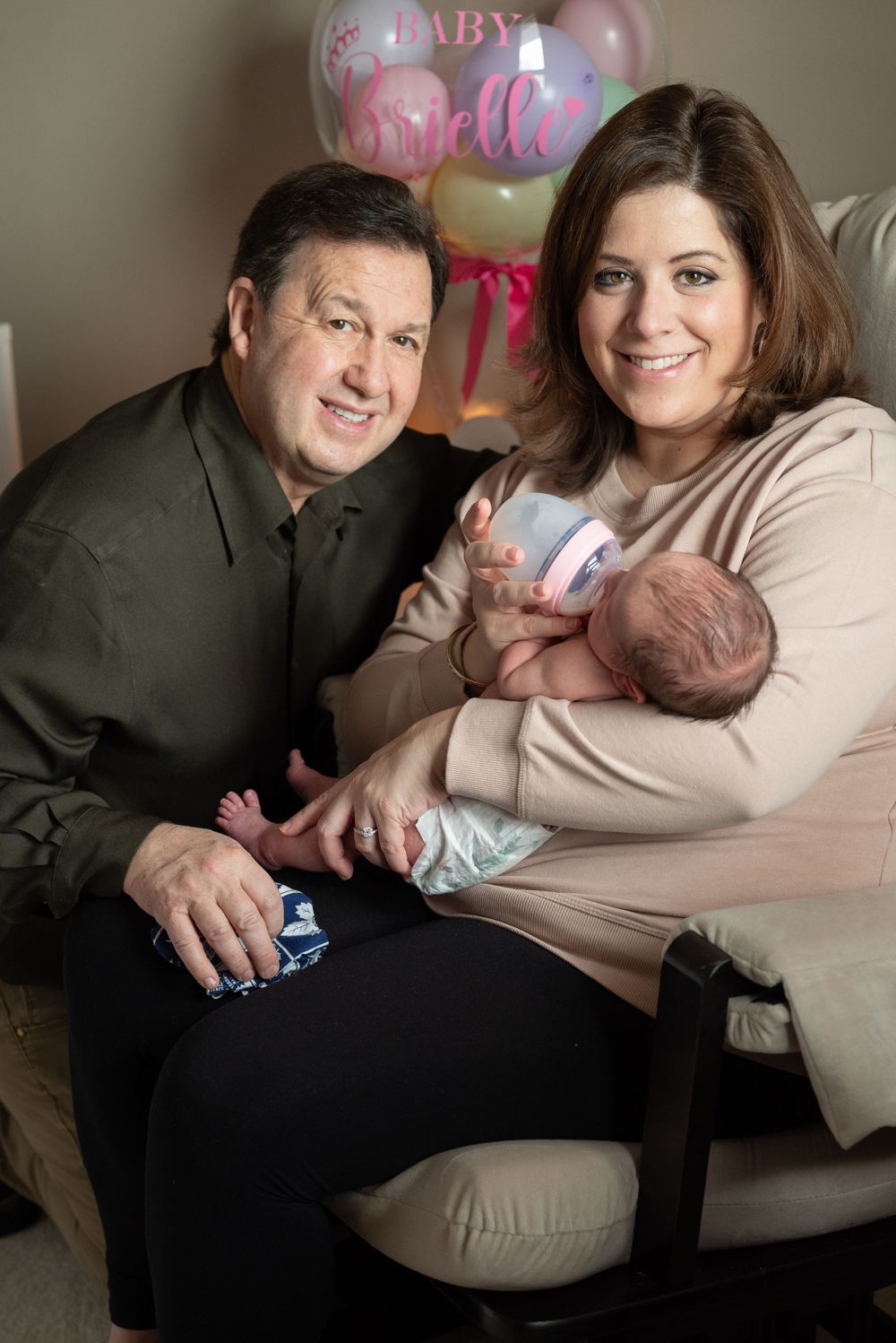 Family portrait with pink baby balloons in background showing tender moment with newborn.
