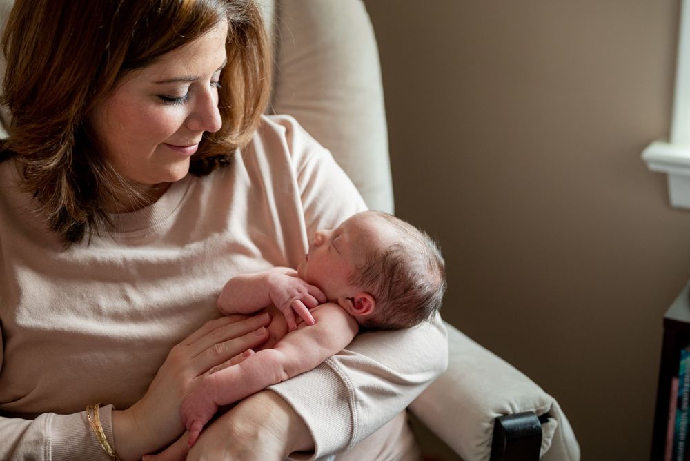 Parent gently holding sleeping newborn in white rocking chair.