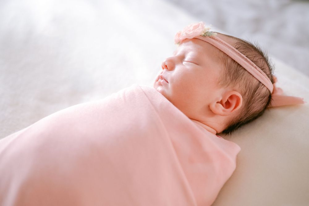 Newborn sleeping in pink wrap with delicate lace headband.
