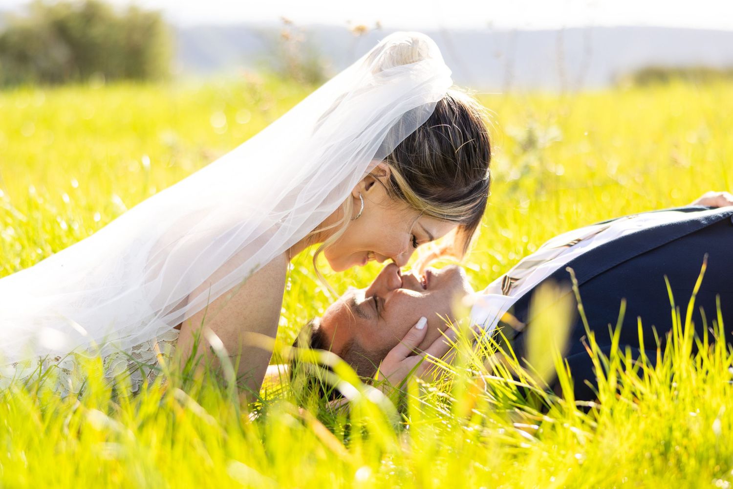 Romantic moment captured in golden meadow with flowing white veil.