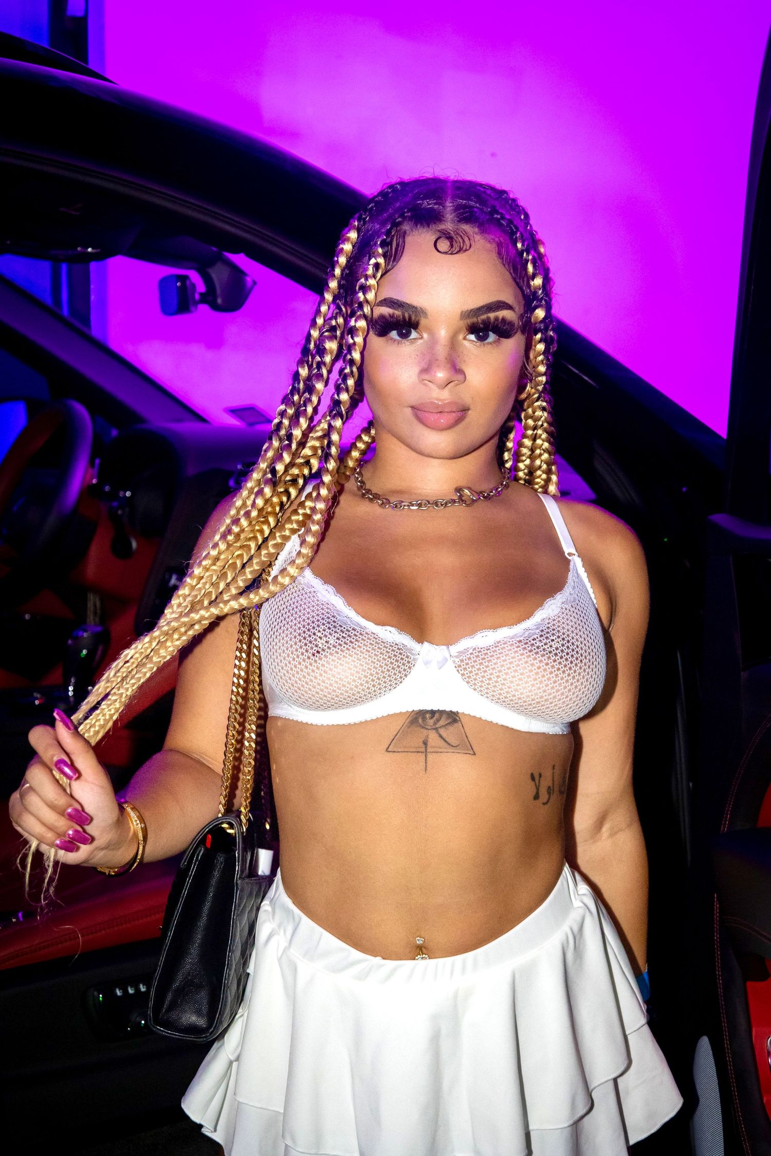 Fashion portrait with braided hair and white outfit against purple lighting.