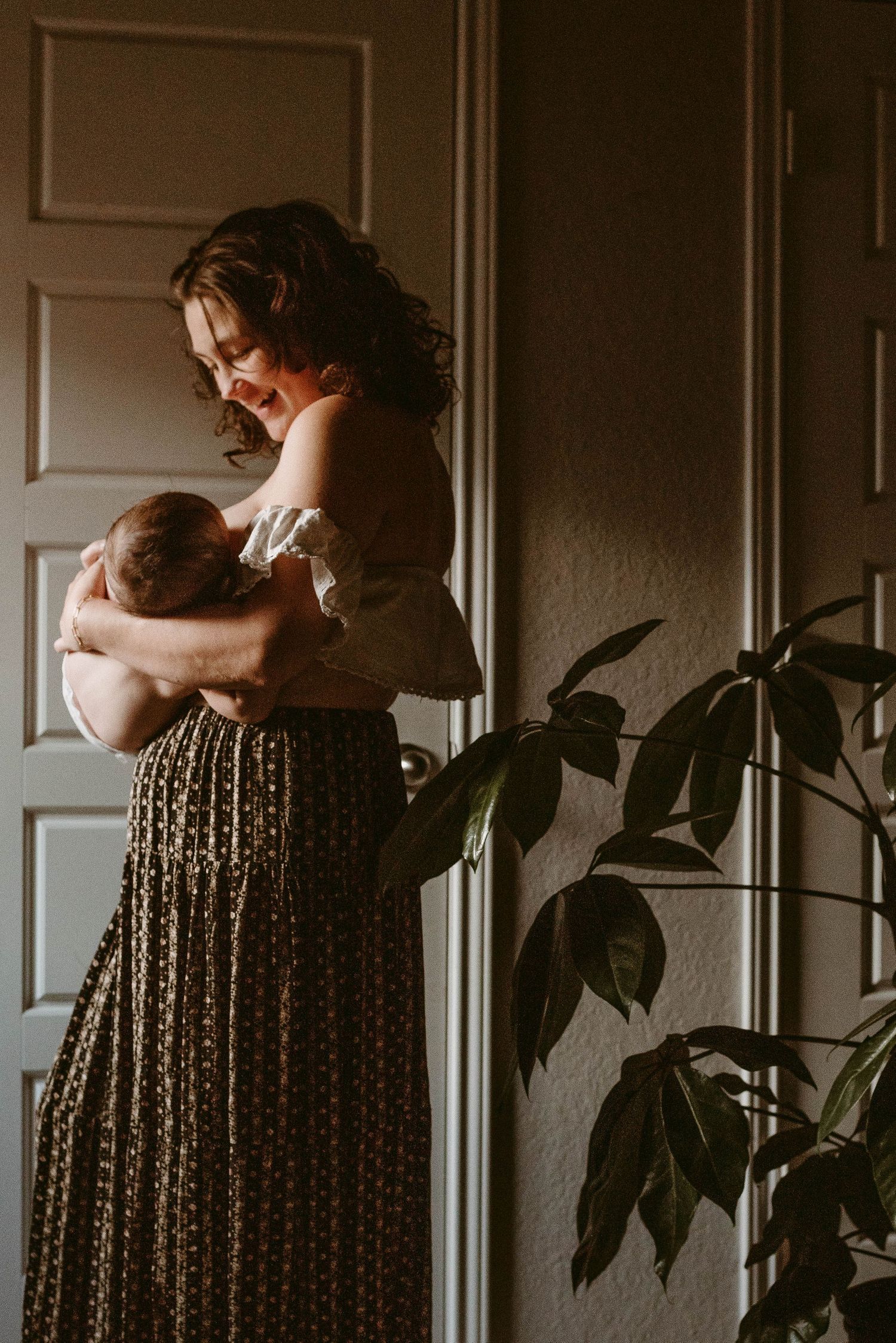 Intimate motherhood portrait showing tender moment between mother and baby in dim natural light.